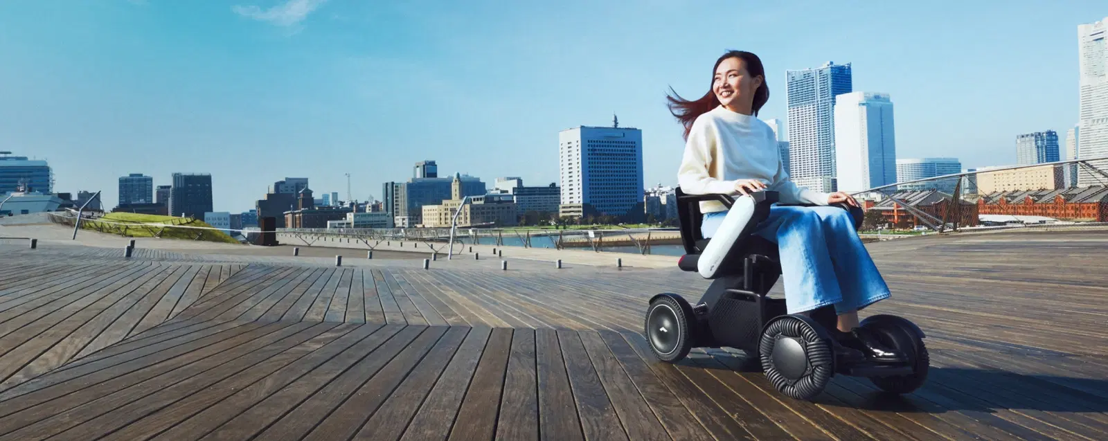 Woman riding a WHILL Model C2 on a waterfront boardwalk