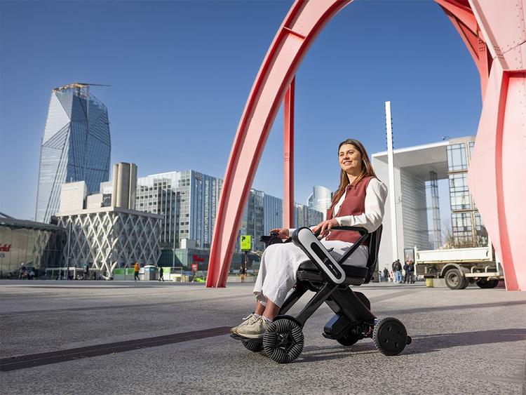 Eine Frau fährt das WHILL Model C Lite auf modernem Stadtplatz im urbanen Umfeld