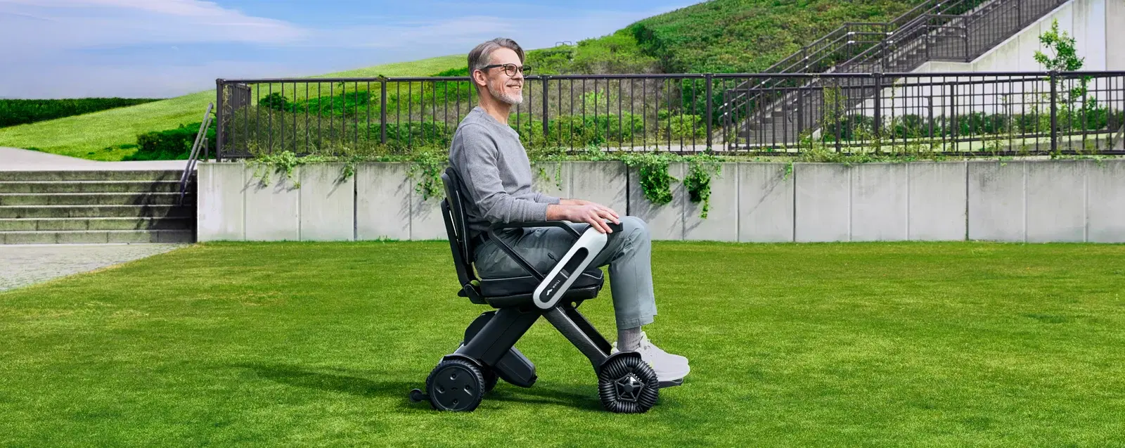 Man seated in a WHILL Model C Lite on a park lawn