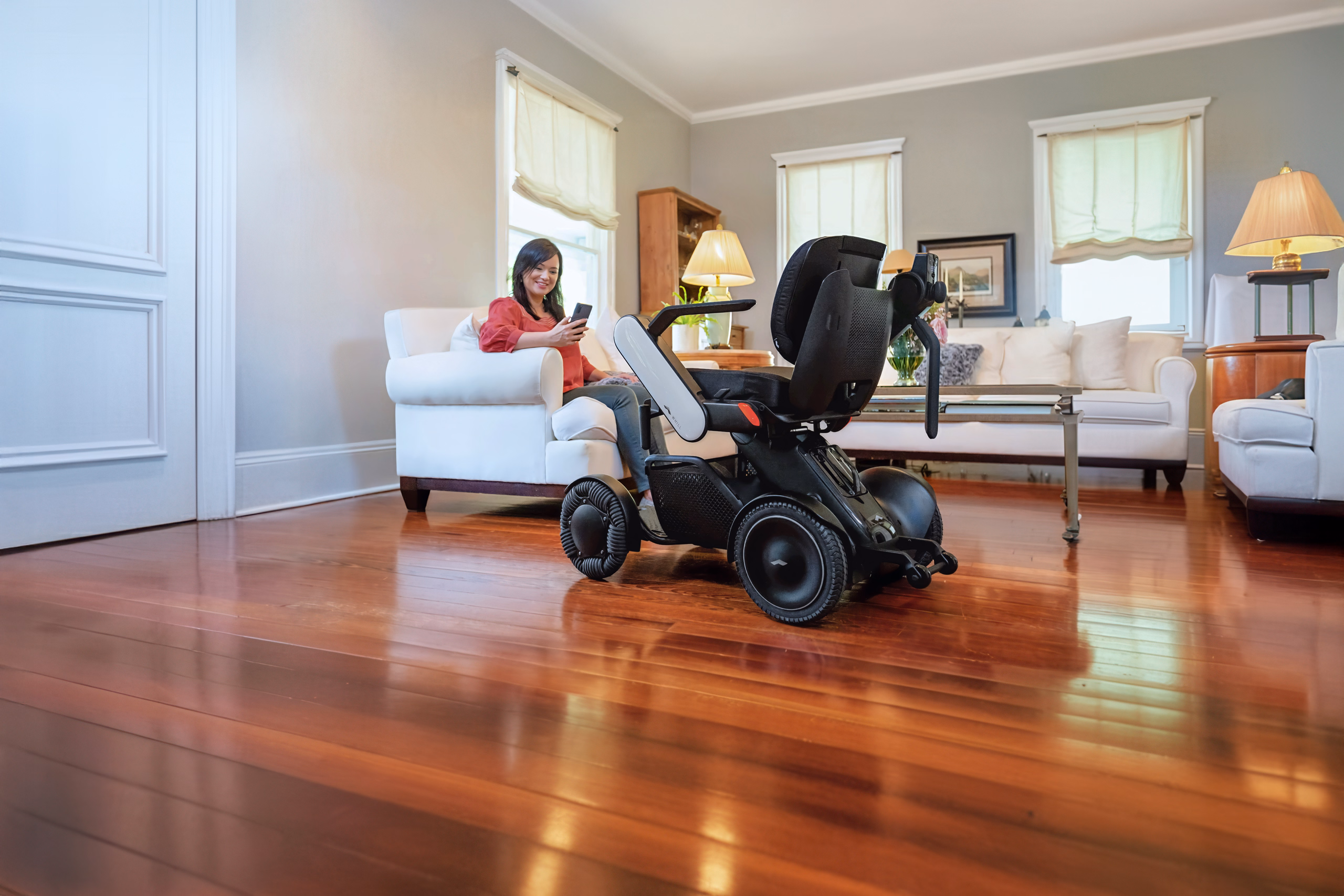 Women sitting on a couch in next to a WHILL Model C2 powerchair.