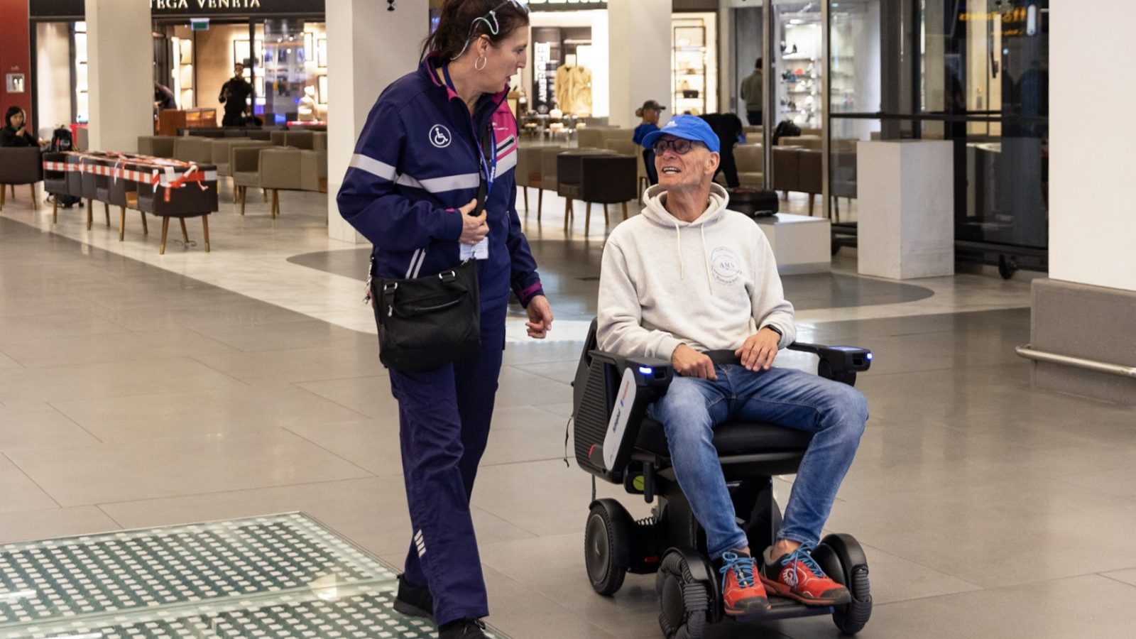 Man on power chair uses WHILL Autonomous Mobility Service to navigate airport.