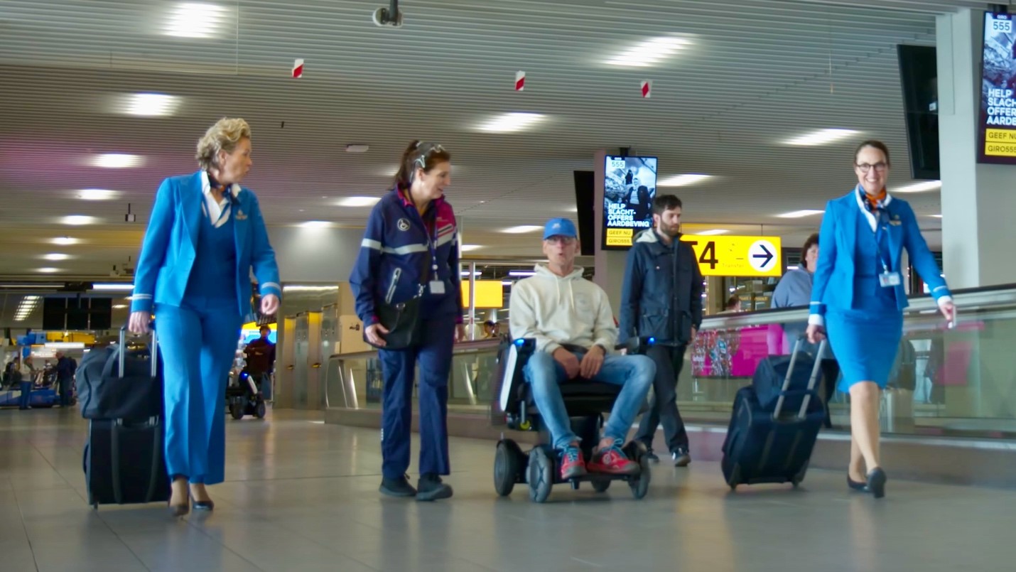 People walk through the airport with a man in a powerchair 
